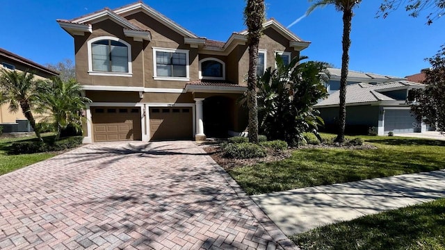 view of front facade with stucco siding, central air condition unit, decorative driveway, a front yard, and a garage