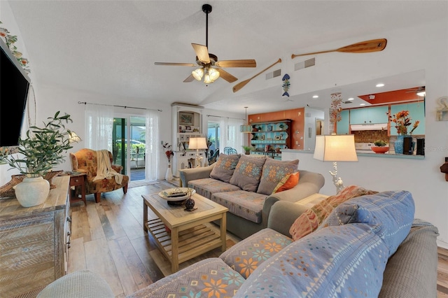 living room with light wood-type flooring, ceiling fan, visible vents, and vaulted ceiling