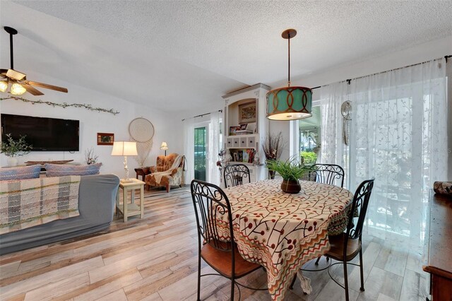 dining room with lofted ceiling, light wood finished floors, a ceiling fan, and a textured ceiling