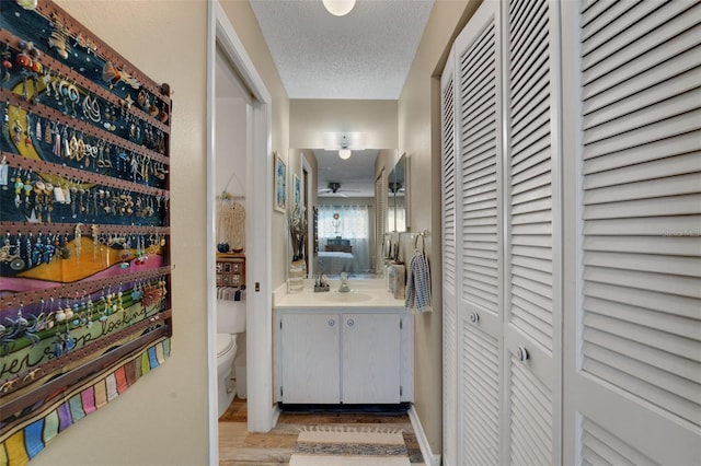 bathroom with a closet, toilet, a textured ceiling, vanity, and wood finished floors