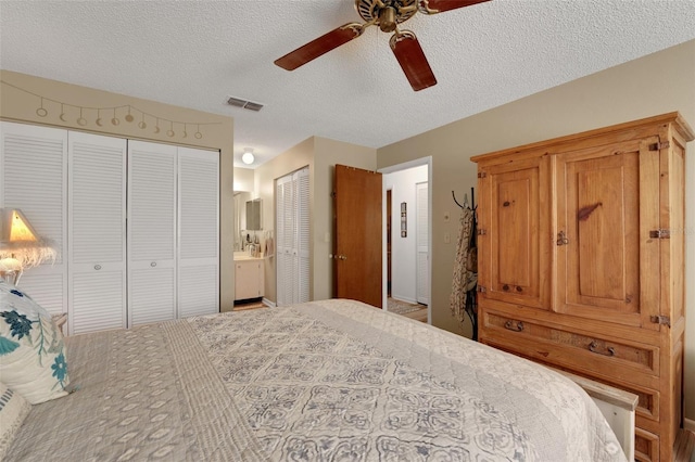 bedroom featuring a ceiling fan, a textured ceiling, visible vents, and two closets