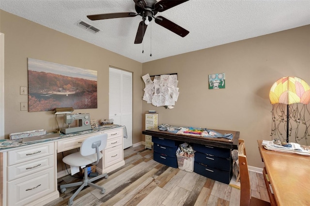 office featuring light wood finished floors, visible vents, ceiling fan, a textured ceiling, and baseboards