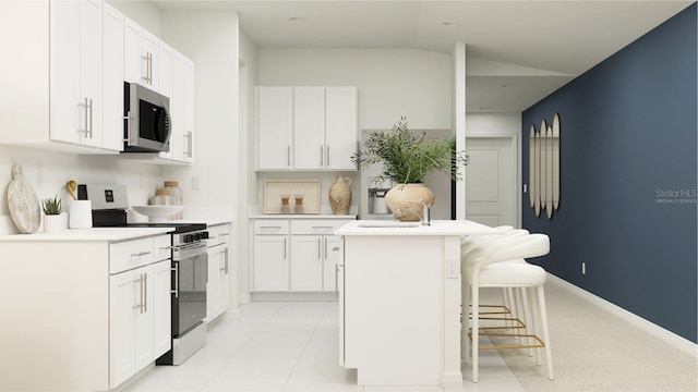 kitchen featuring white cabinets, vaulted ceiling, appliances with stainless steel finishes, a kitchen bar, and a center island with sink