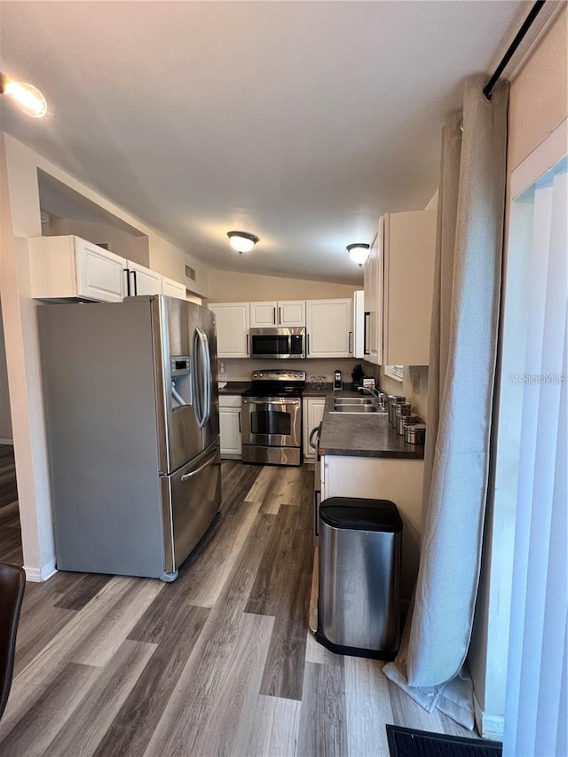 kitchen with dark countertops, appliances with stainless steel finishes, dark wood finished floors, and white cabinets