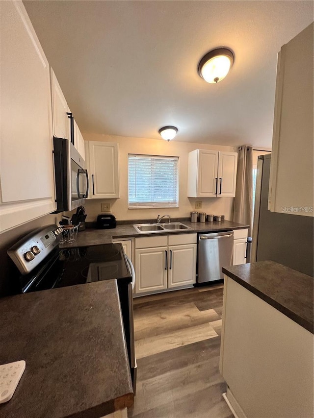 kitchen with stainless steel appliances, dark countertops, a sink, and white cabinets