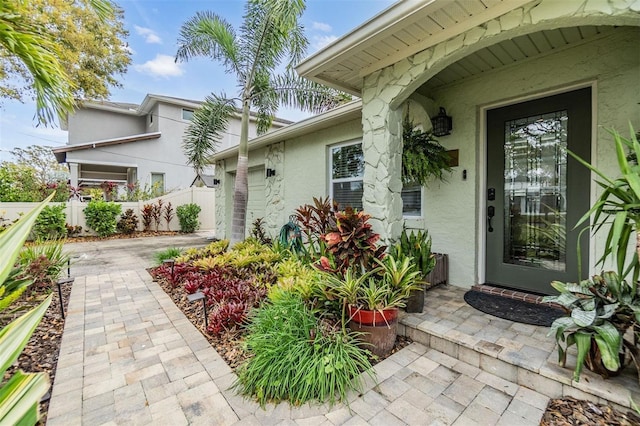 view of exterior entry with a garage, a patio, fence, decorative driveway, and stucco siding