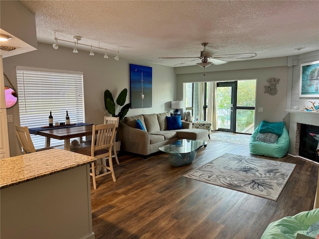 living area with a large fireplace, visible vents, dark wood-style floors, ceiling fan, and a textured ceiling