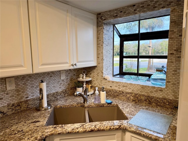 kitchen with tasteful backsplash, white cabinetry, a sink, and light stone countertops