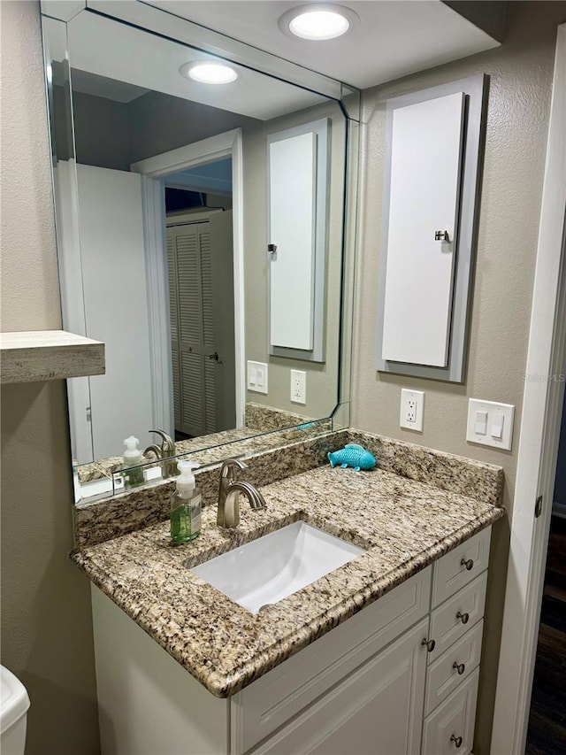 bathroom with a textured wall, recessed lighting, and vanity