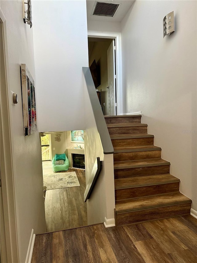 staircase with baseboards, a fireplace, visible vents, and wood finished floors