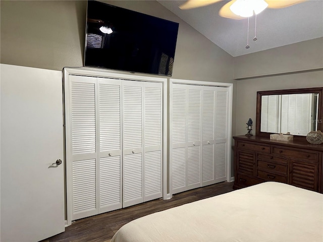 bedroom with multiple closets, dark wood-type flooring, vaulted ceiling, and a ceiling fan