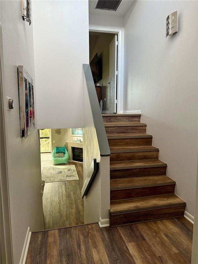 staircase featuring baseboards, a fireplace, visible vents, and wood finished floors