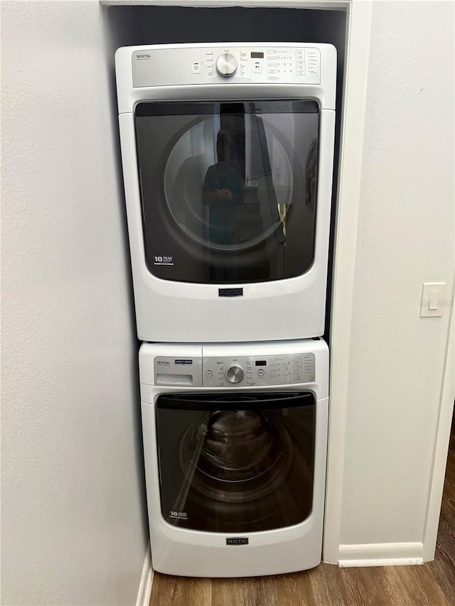 laundry area featuring laundry area, stacked washer / dryer, wood finished floors, and baseboards