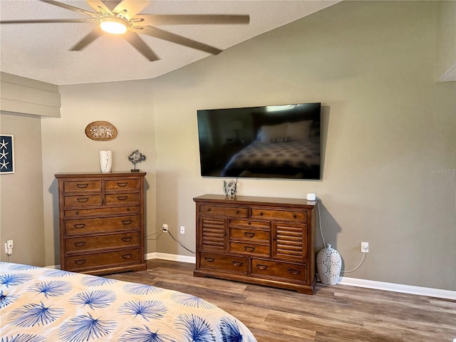 bedroom featuring a ceiling fan, vaulted ceiling, a textured ceiling, wood finished floors, and baseboards