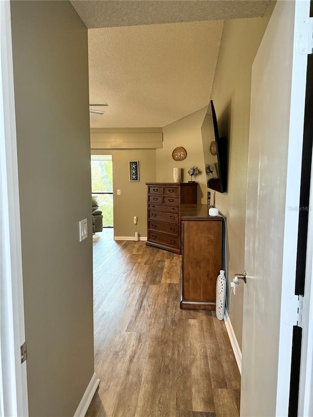 corridor with a textured ceiling, baseboards, and wood finished floors