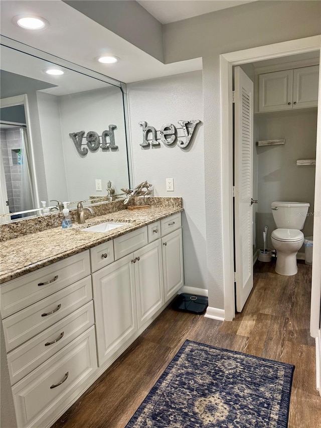 bathroom with baseboards, toilet, wood finished floors, vanity, and recessed lighting