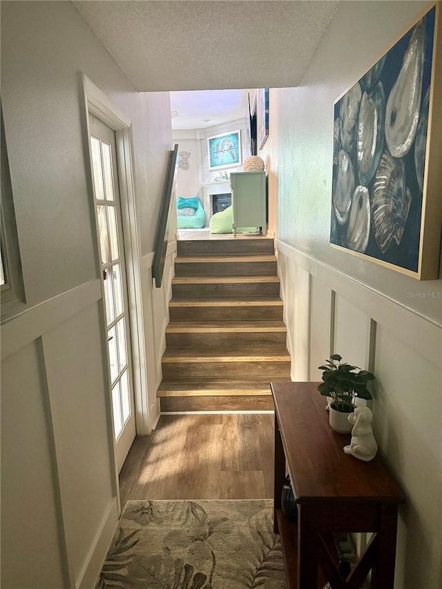 stairway featuring a textured ceiling, a wainscoted wall, wood finished floors, and a decorative wall