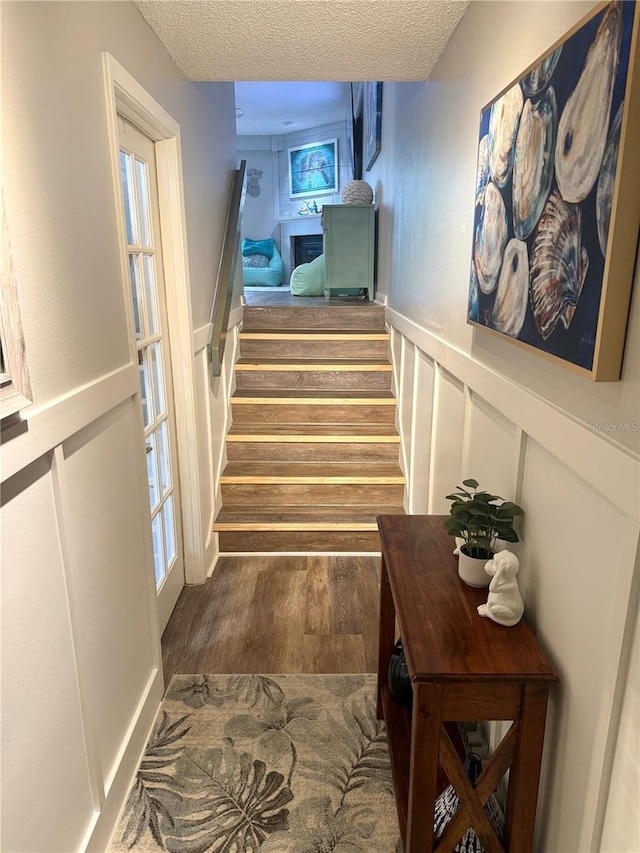 staircase featuring a wainscoted wall, a decorative wall, a textured ceiling, and wood finished floors