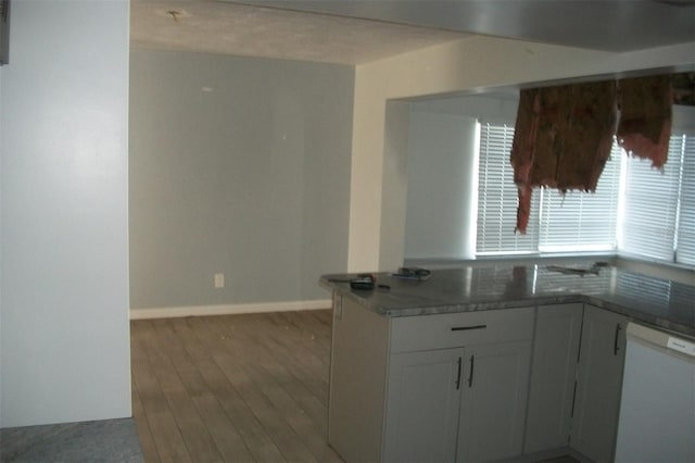 kitchen with baseboards, white dishwasher, wood finished floors, and white cabinets