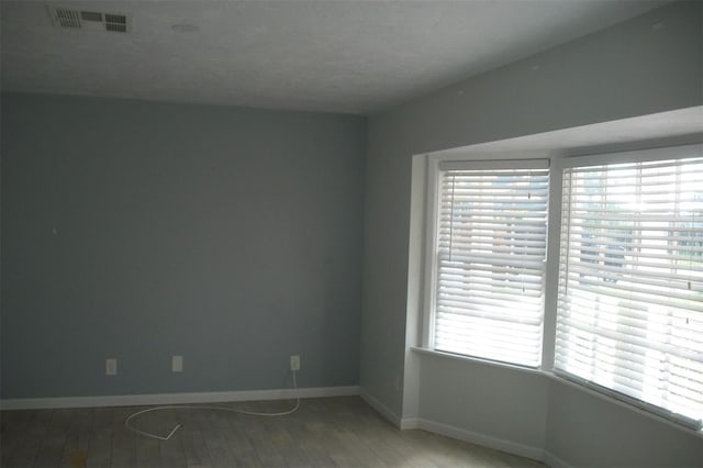 unfurnished room with wood finished floors, visible vents, and baseboards