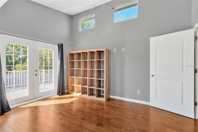 interior space featuring hardwood / wood-style flooring, french doors, baseboards, and a towering ceiling