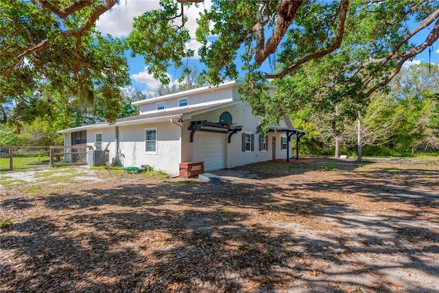 rear view of property with a gate, fence, central AC unit, stucco siding, and a garage