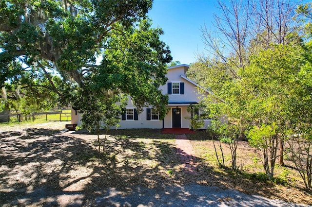 view of property hidden behind natural elements with stucco siding and fence