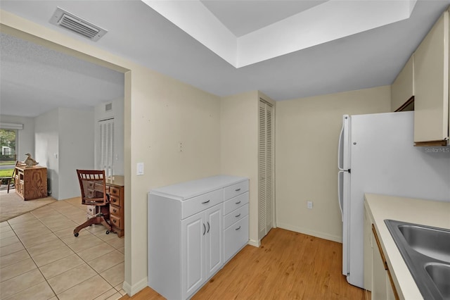 kitchen with a sink, visible vents, white cabinetry, light countertops, and freestanding refrigerator