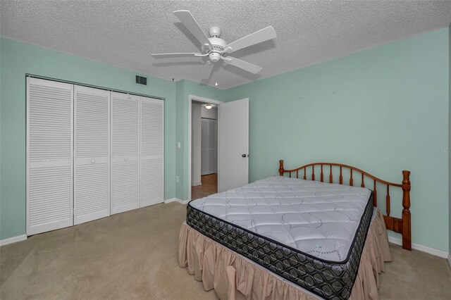 bedroom with a textured ceiling, ceiling fan, light colored carpet, baseboards, and a closet