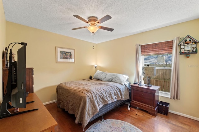 bedroom featuring ceiling fan, a textured ceiling, baseboards, and wood finished floors