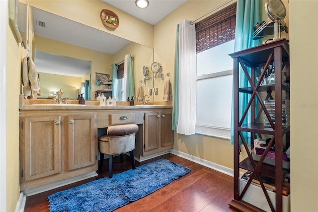 bathroom with double vanity, visible vents, a sink, wood finished floors, and baseboards