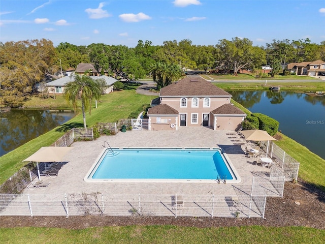 community pool with a lawn, a patio area, fence, and a water view