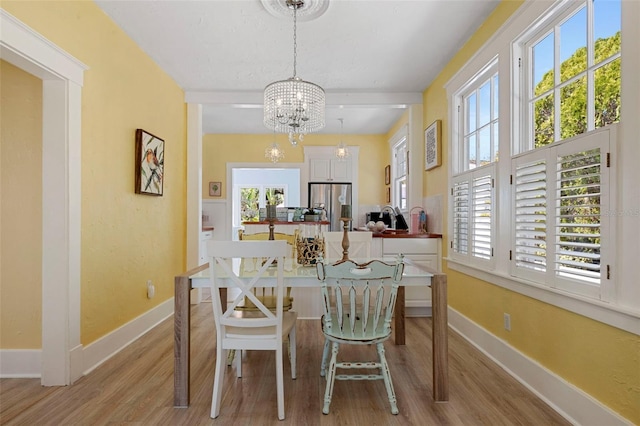 dining space with beamed ceiling, light wood-type flooring, an inviting chandelier, and baseboards