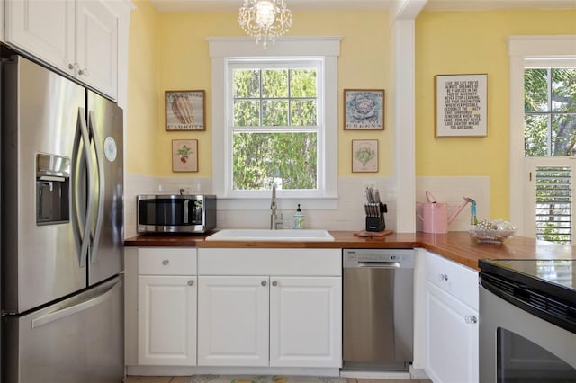 kitchen with appliances with stainless steel finishes, a sink, wood counters, and tasteful backsplash