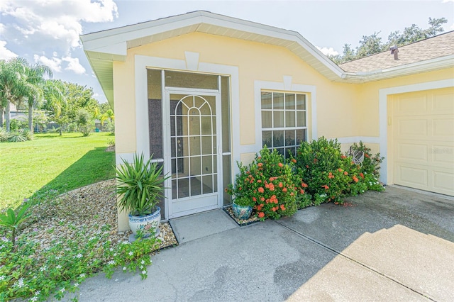 view of exterior entry featuring an attached garage, driveway, roof with shingles, a lawn, and stucco siding