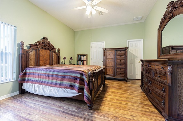 bedroom with a ceiling fan, visible vents, baseboards, and wood finished floors