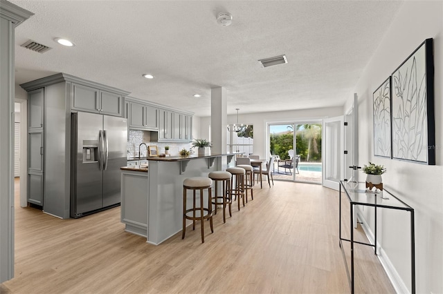 kitchen featuring light wood finished floors, gray cabinets, stainless steel refrigerator with ice dispenser, a kitchen bar, and dark countertops