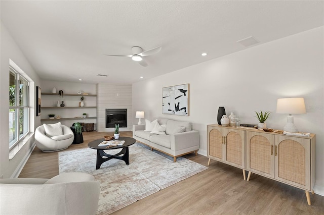 living room with ceiling fan, baseboards, a large fireplace, and wood finished floors