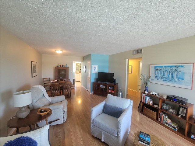 living room with light wood finished floors, visible vents, and a textured ceiling