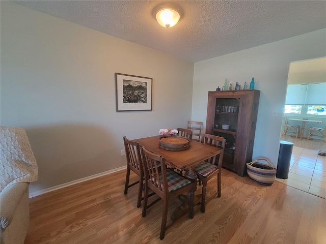 dining space featuring light wood-type flooring, baseboards, and a textured ceiling