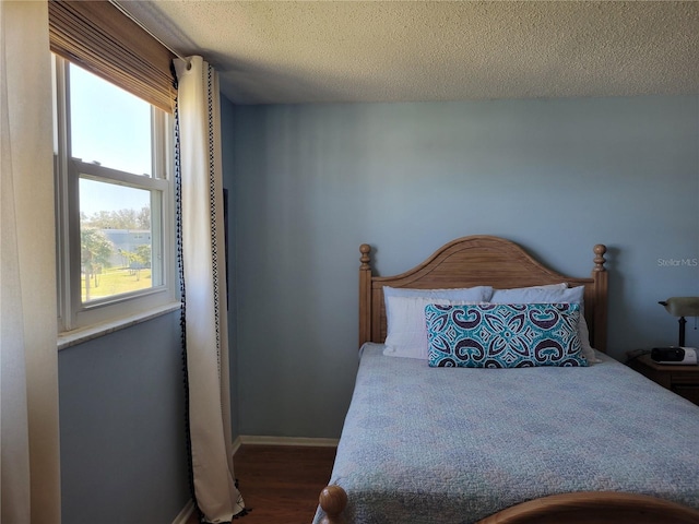 bedroom with a textured ceiling, baseboards, and wood finished floors