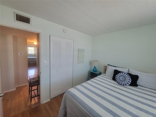 bedroom featuring a closet, visible vents, dark wood finished floors, and a textured ceiling