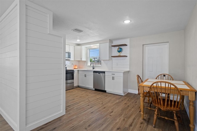 kitchen with wood finished floors, white cabinetry, stainless steel appliances, light countertops, and decorative backsplash