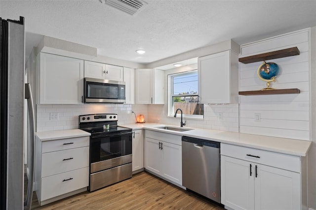 kitchen with visible vents, open shelves, light wood-style flooring, a sink, and appliances with stainless steel finishes