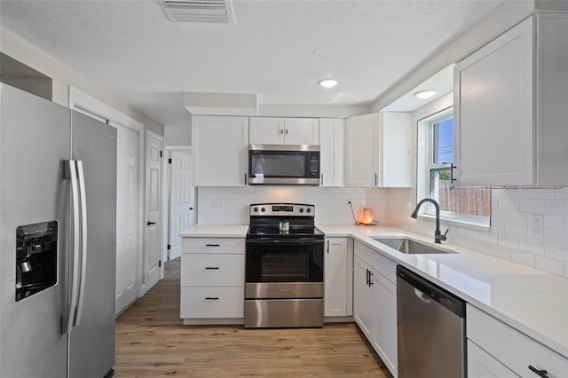 kitchen with light wood-type flooring, visible vents, a sink, appliances with stainless steel finishes, and light countertops