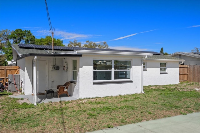 back of property featuring stucco siding, a lawn, roof mounted solar panels, fence, and cooling unit