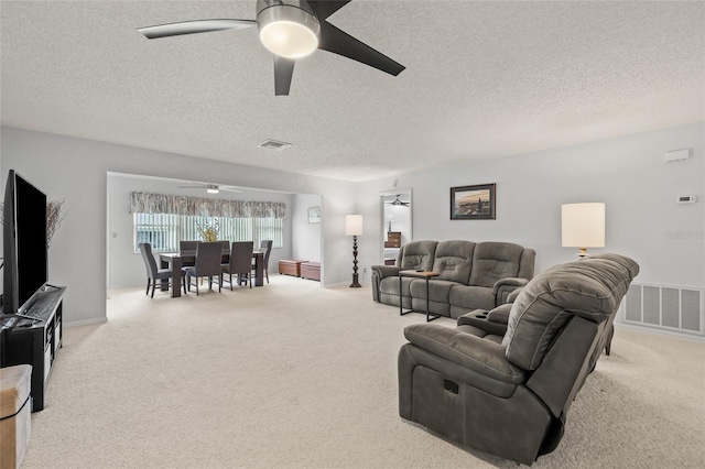 carpeted living area featuring visible vents, a textured ceiling, and a ceiling fan