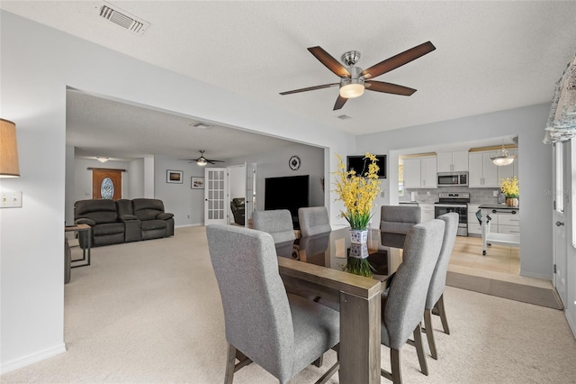 dining room featuring visible vents, light colored carpet, a textured ceiling, and a ceiling fan