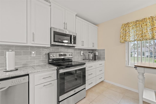 kitchen with light stone countertops, light tile patterned flooring, appliances with stainless steel finishes, white cabinetry, and tasteful backsplash