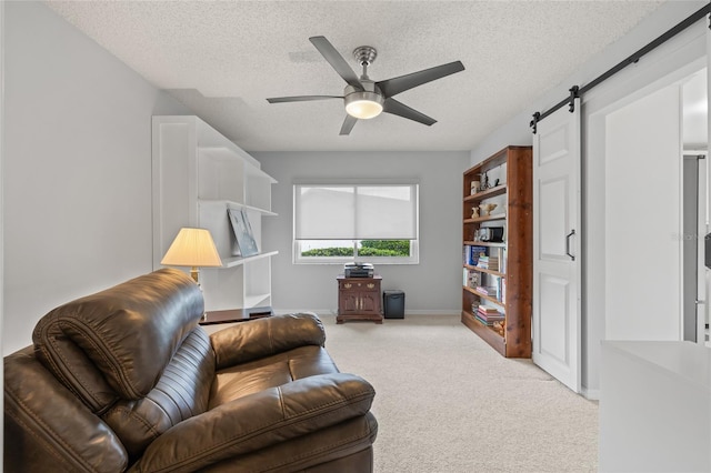 living area with a ceiling fan, a barn door, light colored carpet, and a textured ceiling